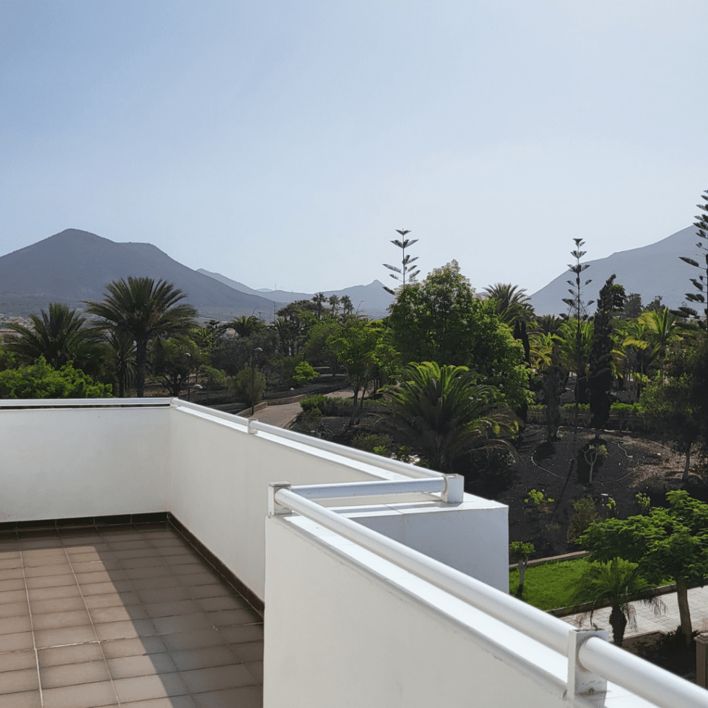 Balcony views from my top floor 2 bedroom apartment at Whala! Tenerife. you can see greenery and mountains in the background behind a white balcony wall.